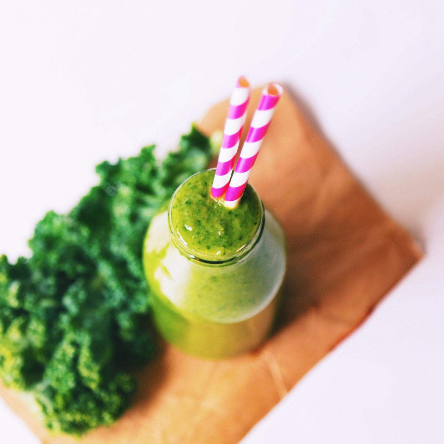 Green smoothie with a striped straw next to kale