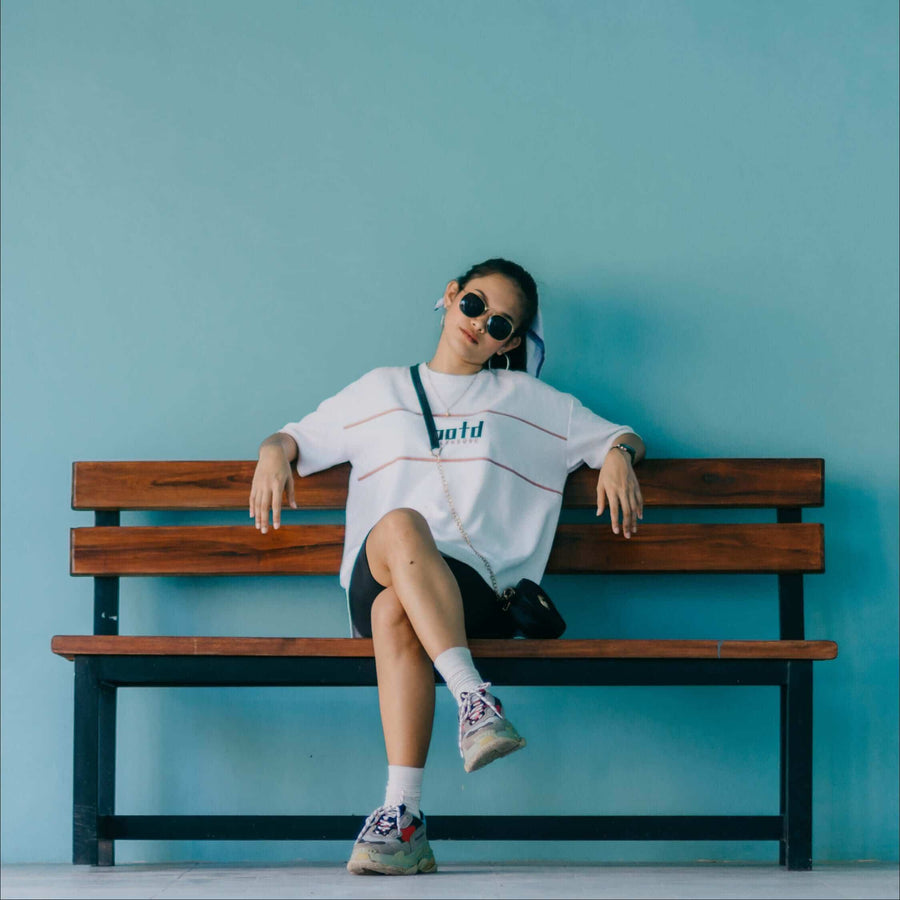 Woman in sunglasses sitting on a bench against a blue wall