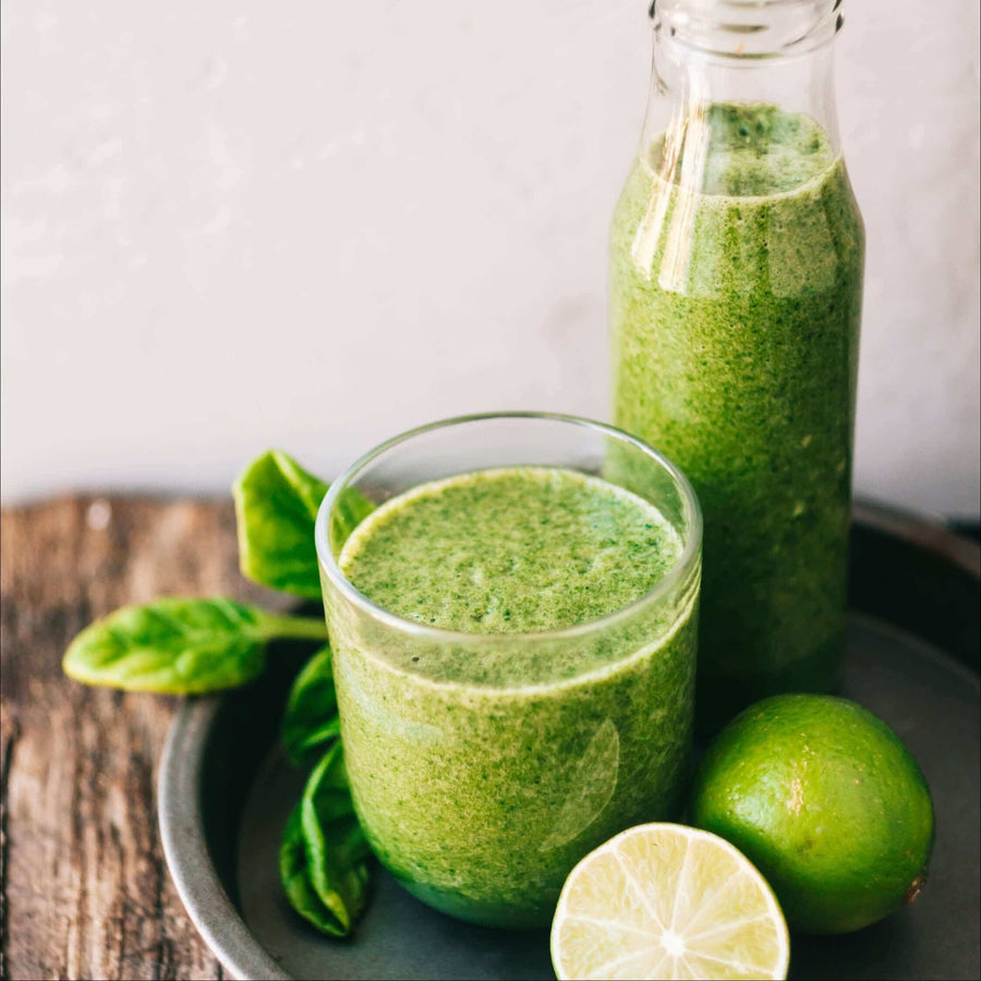 Green smoothie in a glass and bottle with lime and spinach