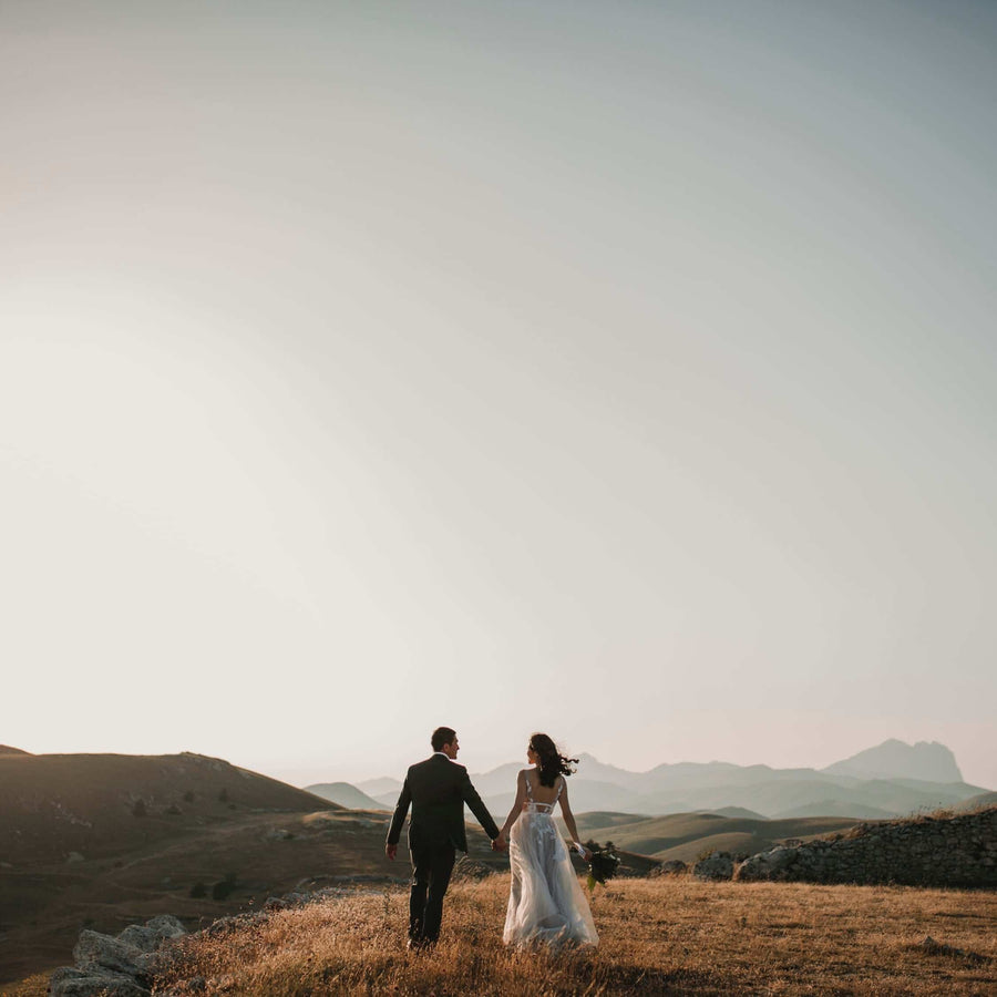 Couple walking hand in hand across hills at sunset