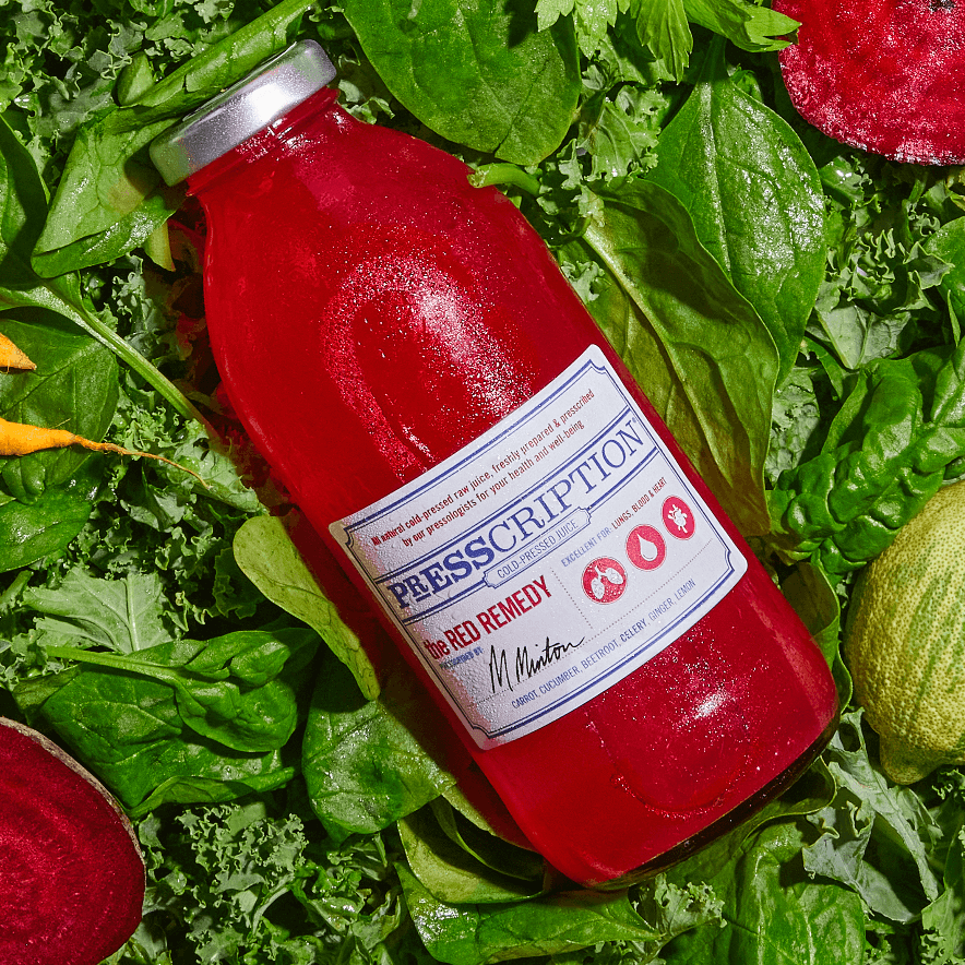 Bottle of The Red Remedy juice lying on spinach leaves and beetroot