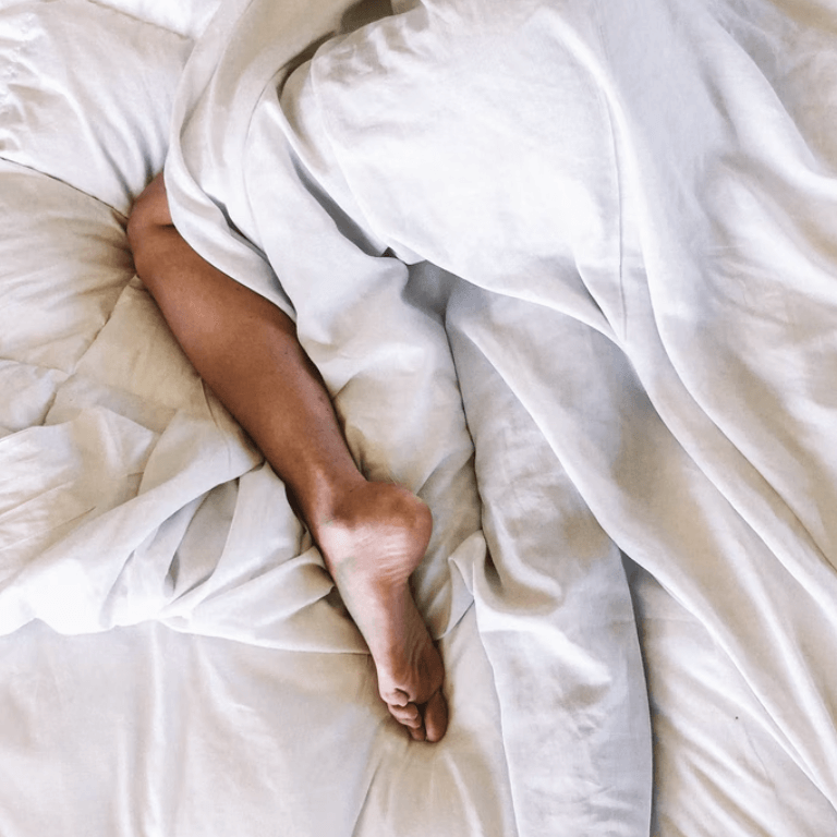 Foot resting on rumpled white bedsheets