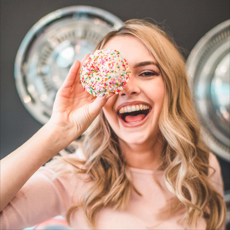 Smiling woman holding a sprinkle doughnut over one eye