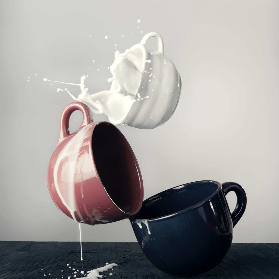 Two cups with milk splashing between them