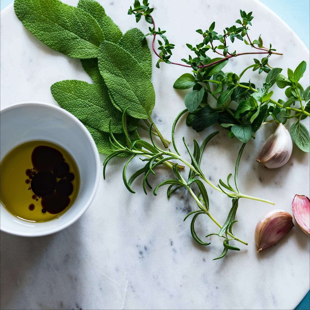 Fresh herbs, garlic and a bowl of olive oil on marble